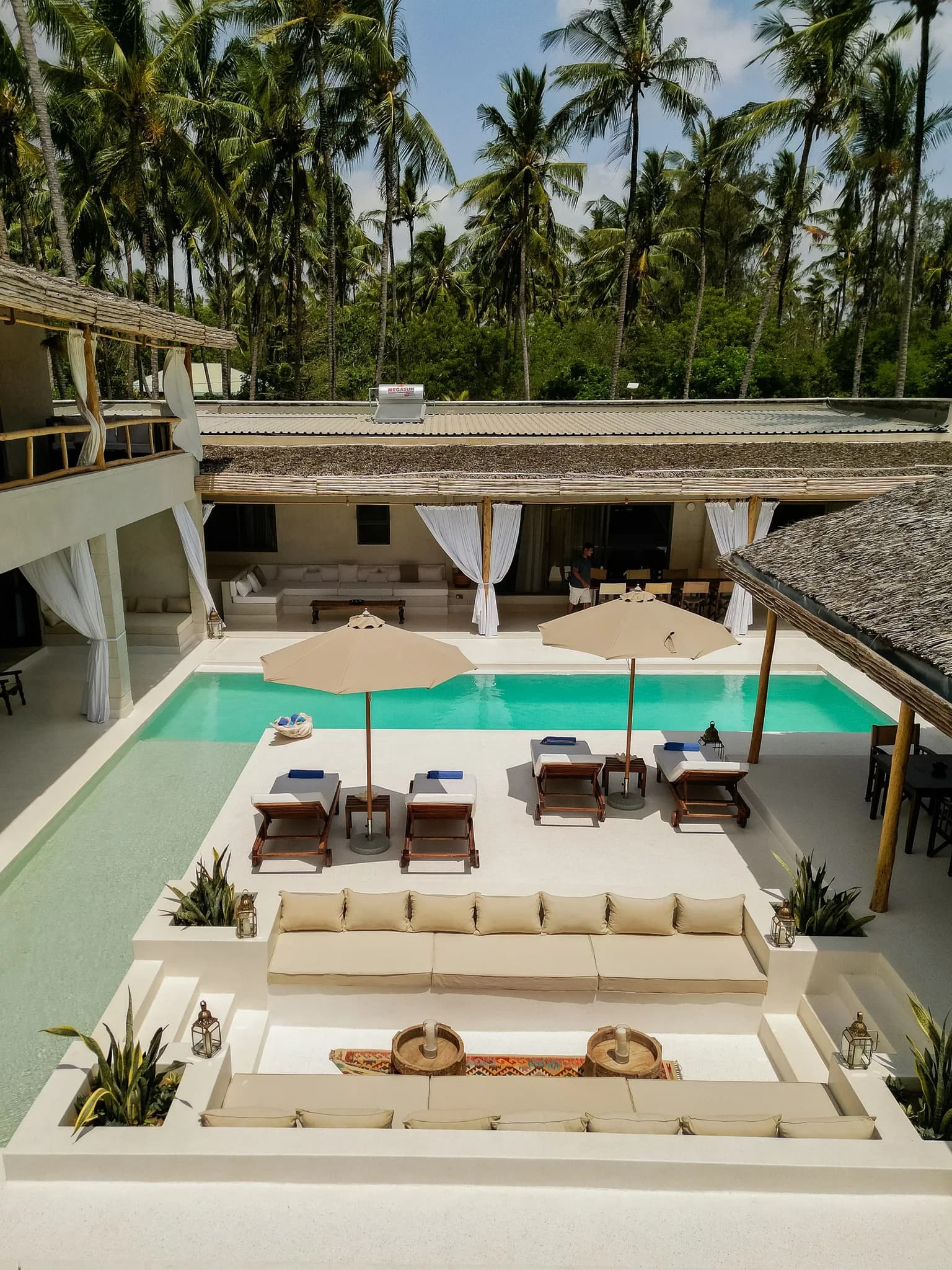 A luxurious tropical villa features an infinity pool, lounge seating, and palm trees under a sunny sky, evoking a serene and relaxing mood.