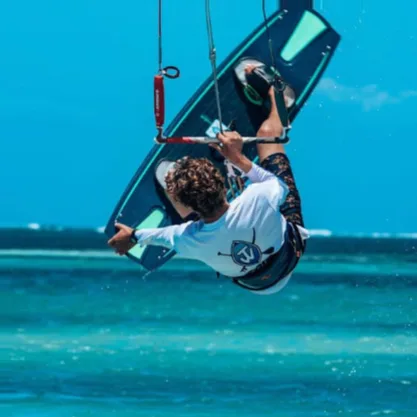 A young man kitesurfs dynamically over turquoise ocean waters under a clear blue sky, conveying excitement and freedom.